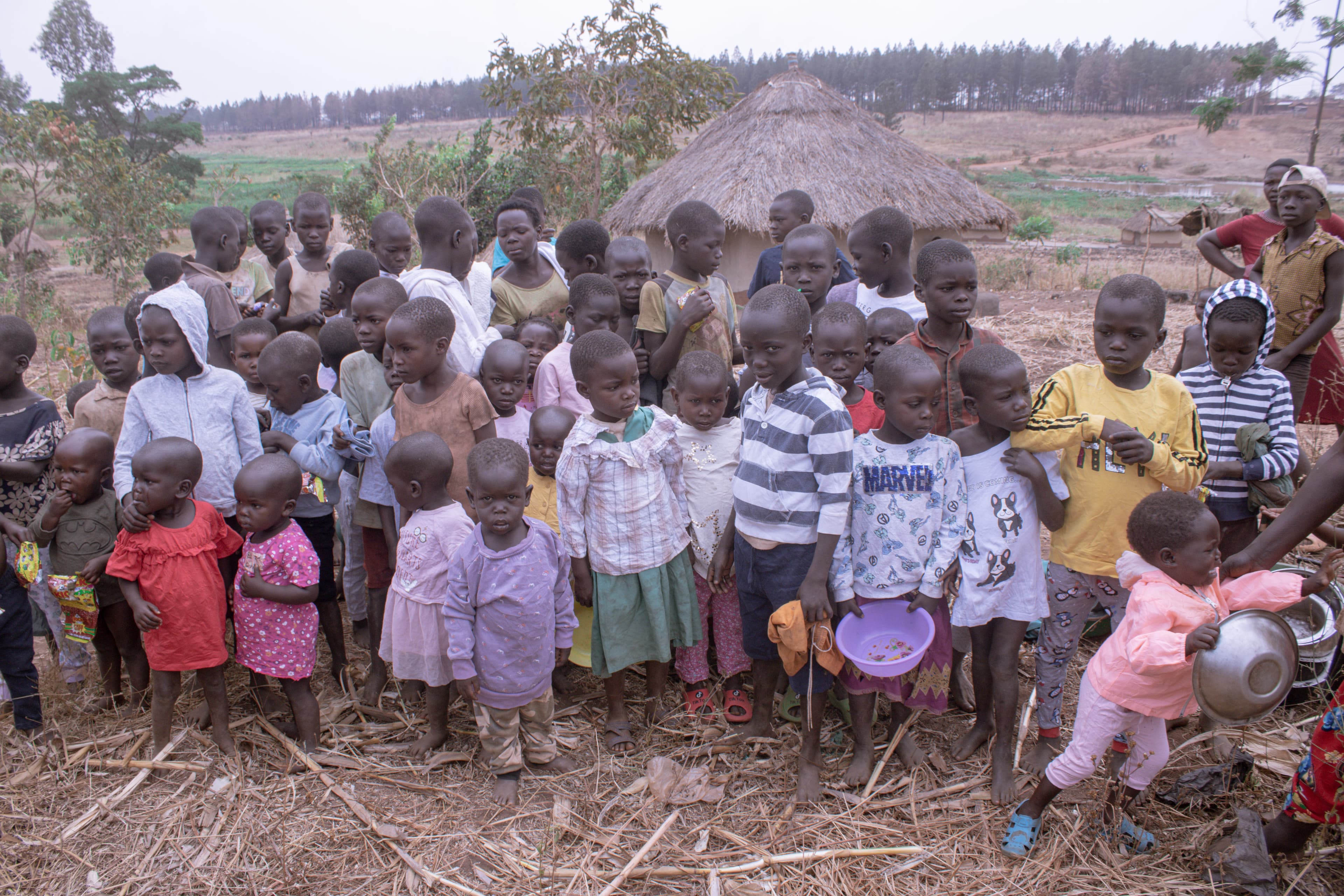 A large group of children gathered outdoors on a hillside near the village.