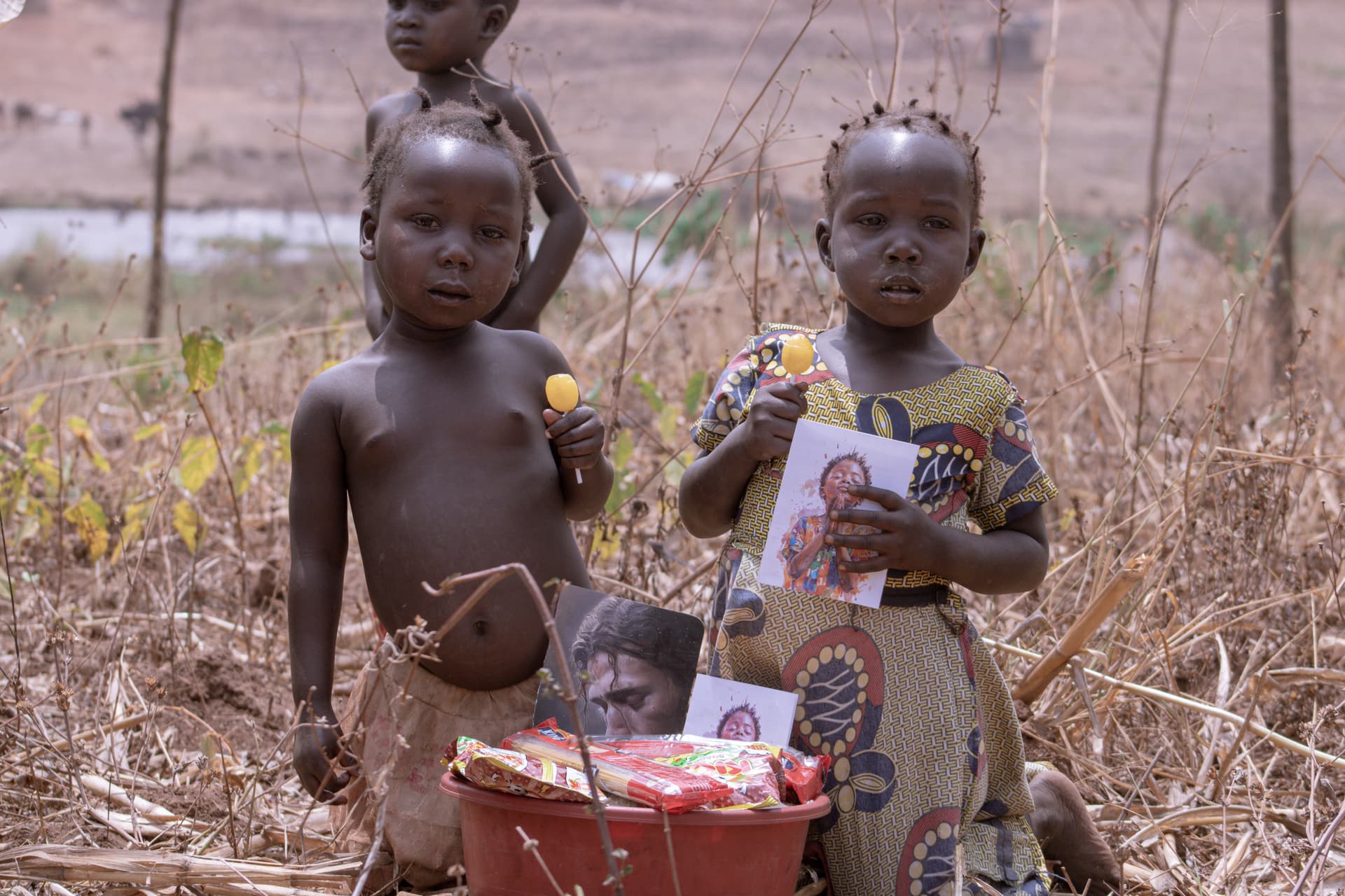 Two young children outdoors hold a devotional card and a small red basket.