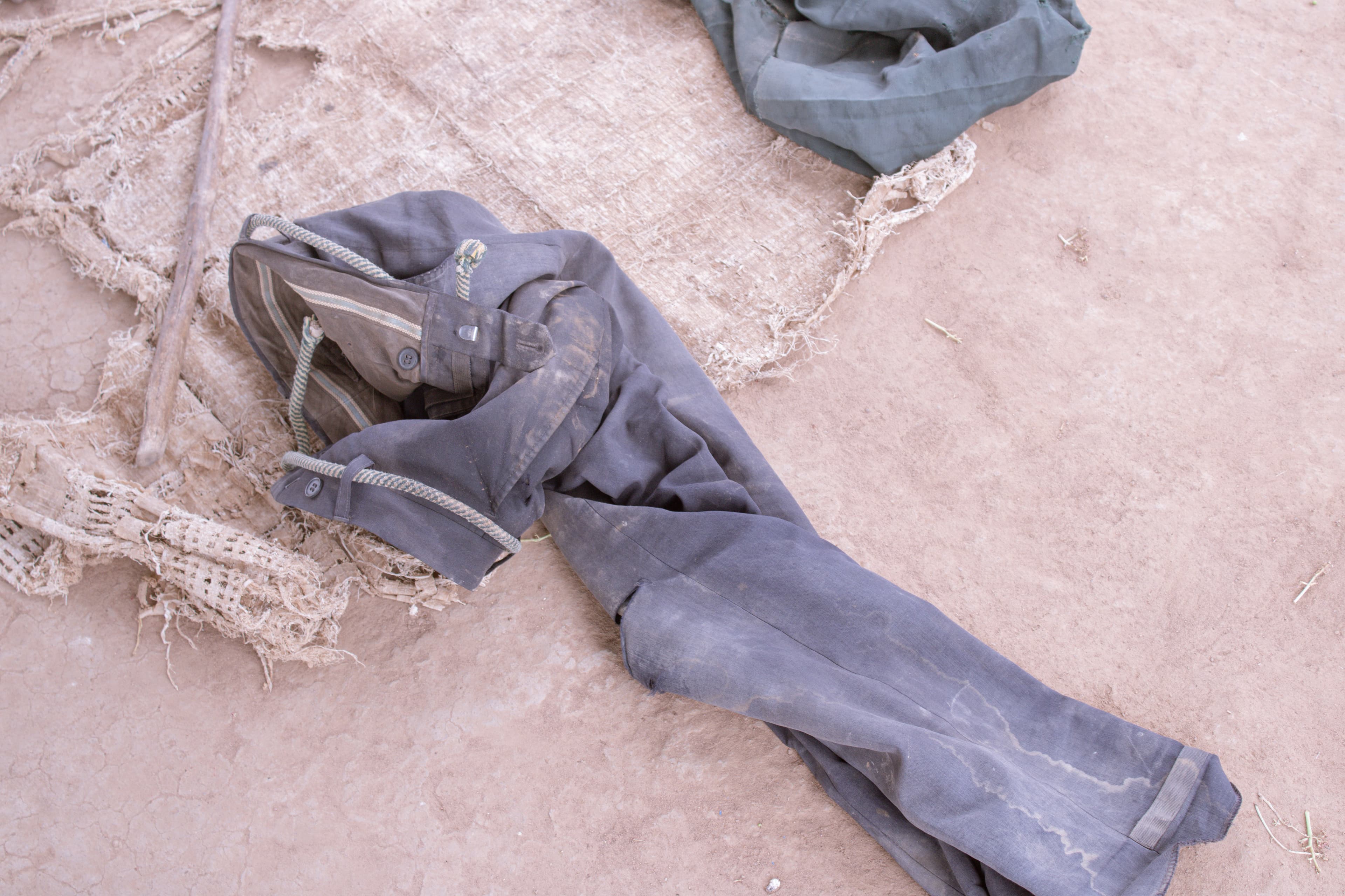 Worn, torn dark clothing and shoes laid on the bare ground.