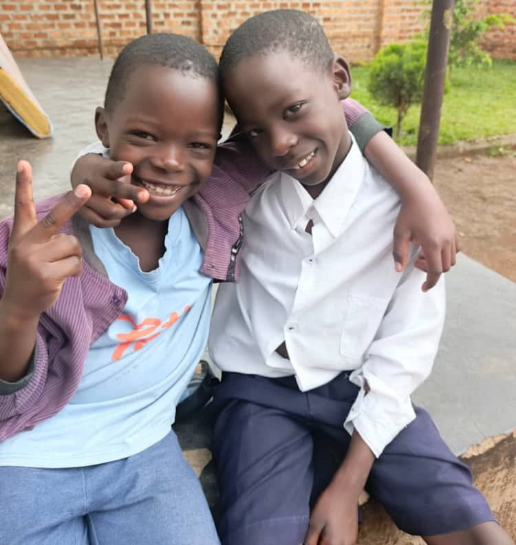 Two boys in school uniforms with arms around each other, smiling for the camera.