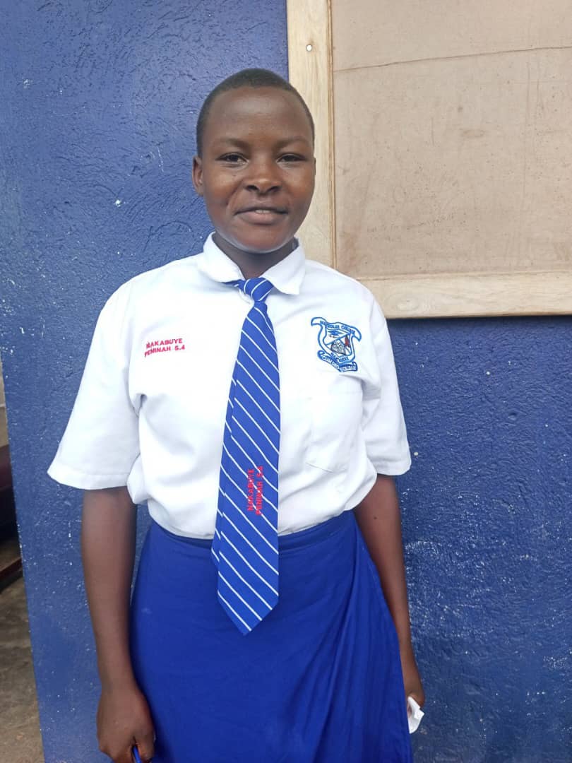 Girl in a blue school uniform with a tie, standing indoors.