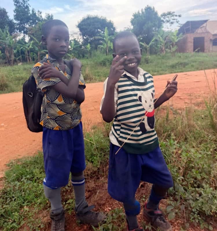 Two boys wearing backpacks standing together, one making a peace sign.