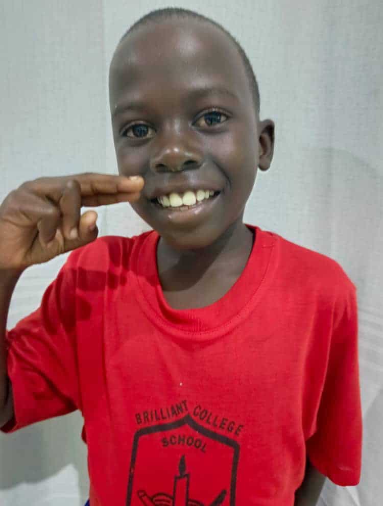 Boy in a red shirt giving a thumbs up to the camera.