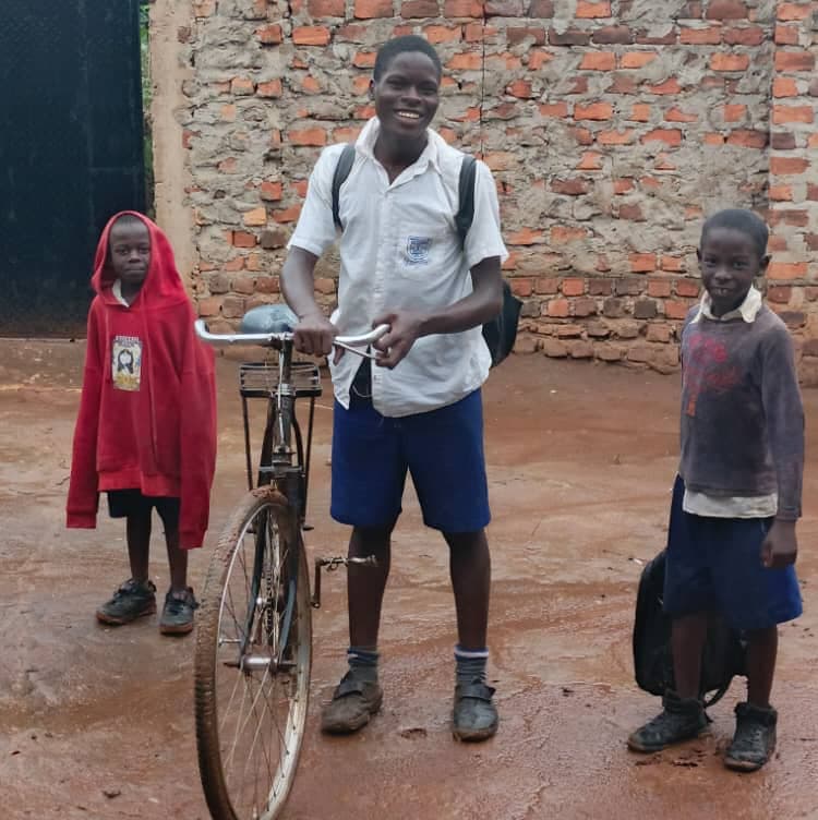 Girl in a red top standing with a boy in a school uniform beside a bicycle.
