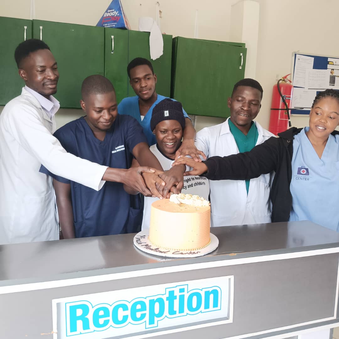 Miracle Medical Center staff in scrubs gather around a cake at the reception desk to celebrate.