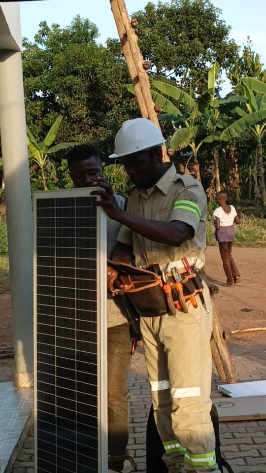 A worker in a hard hat carries a solar panel beside a building.