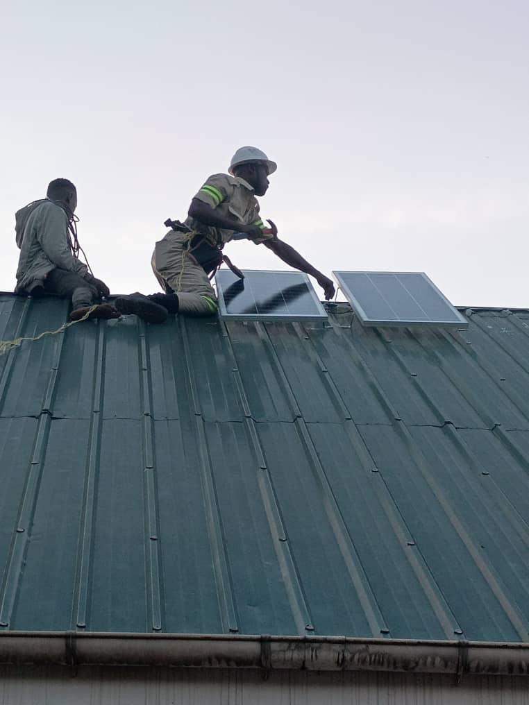 Two workers install solar equipment on a metal roof.
