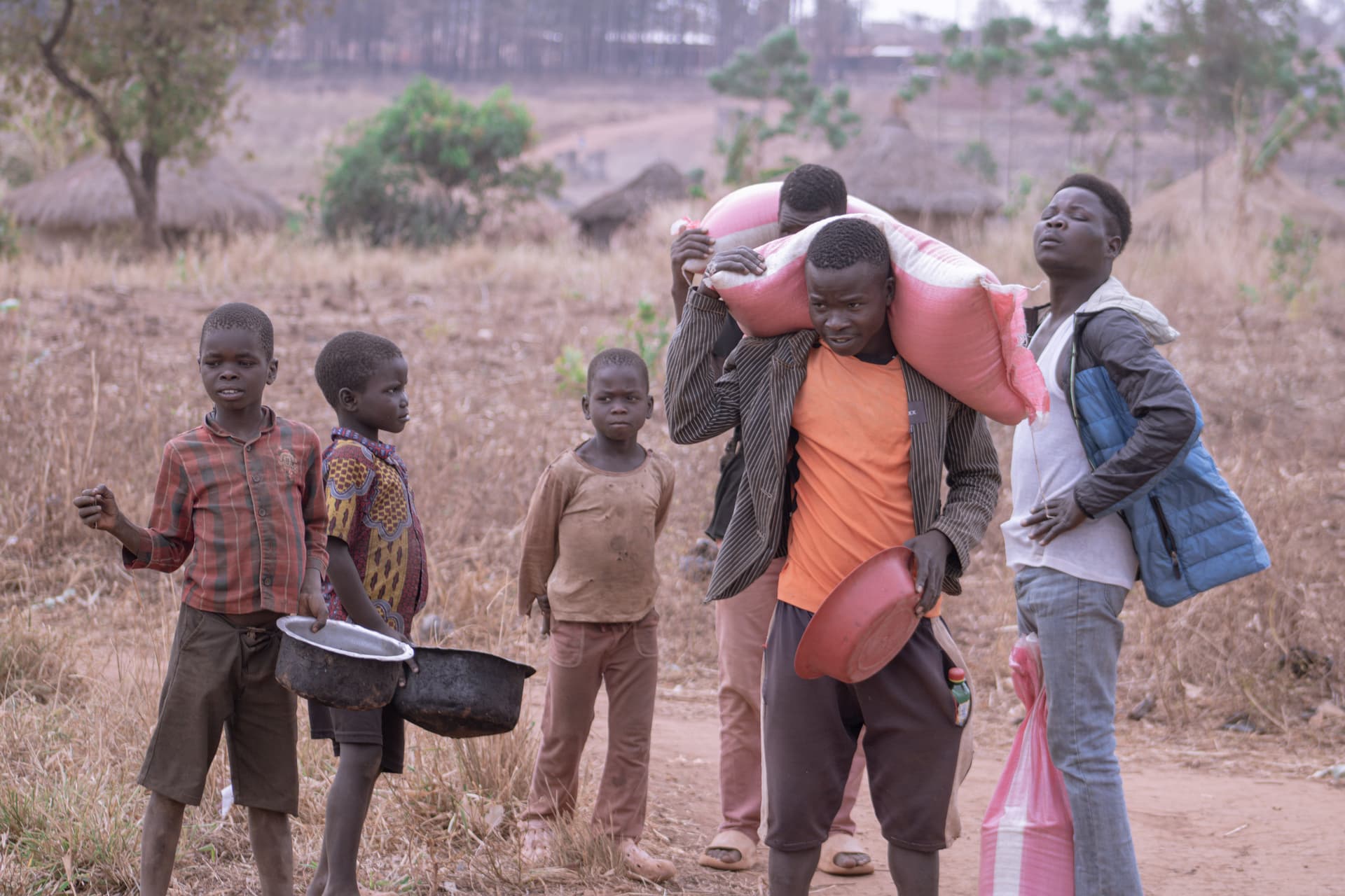 A small group of children standing together along a dirt path with one raising an arm.