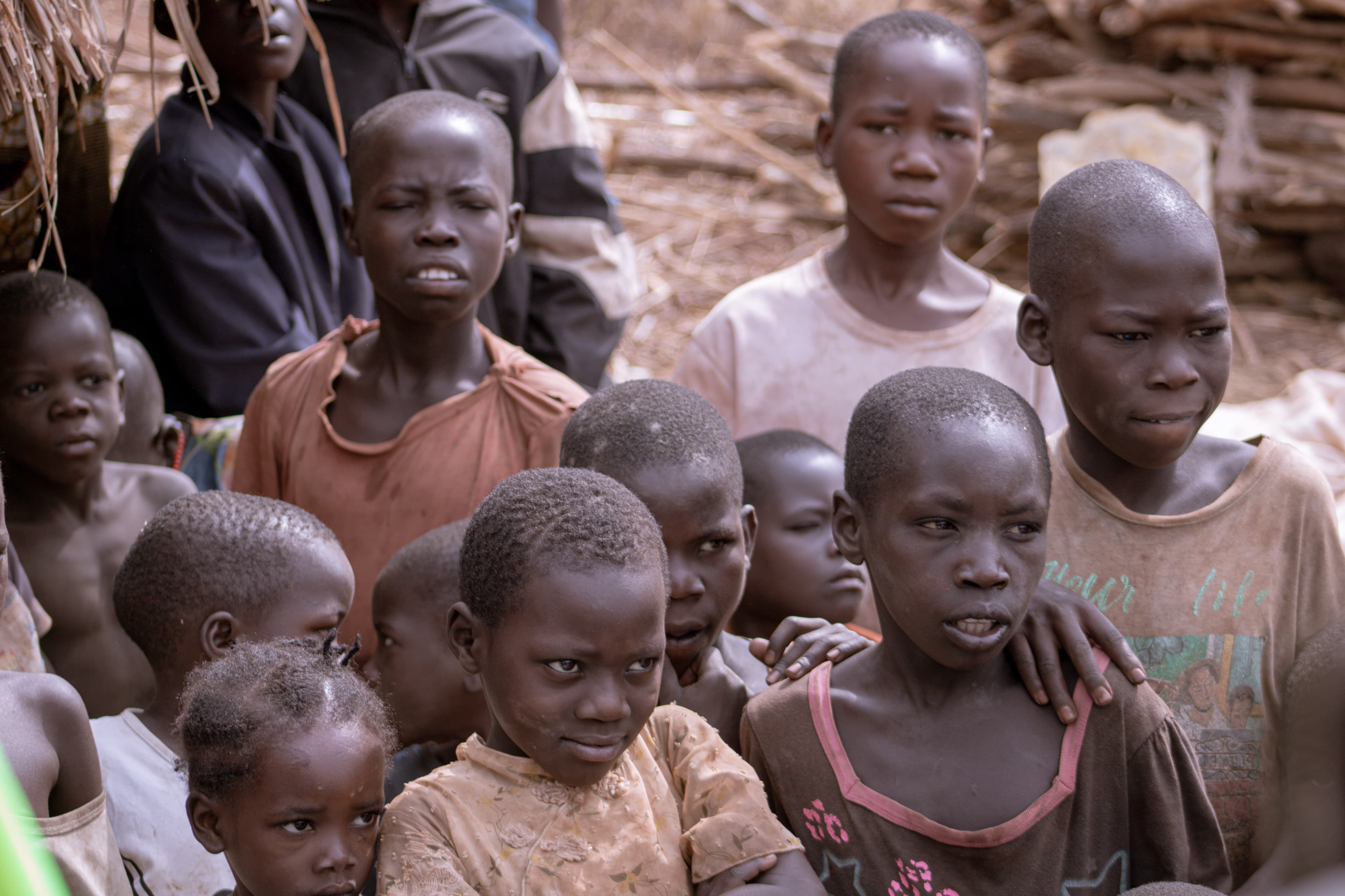 Group of children standing close together outdoors, some in worn clothing.