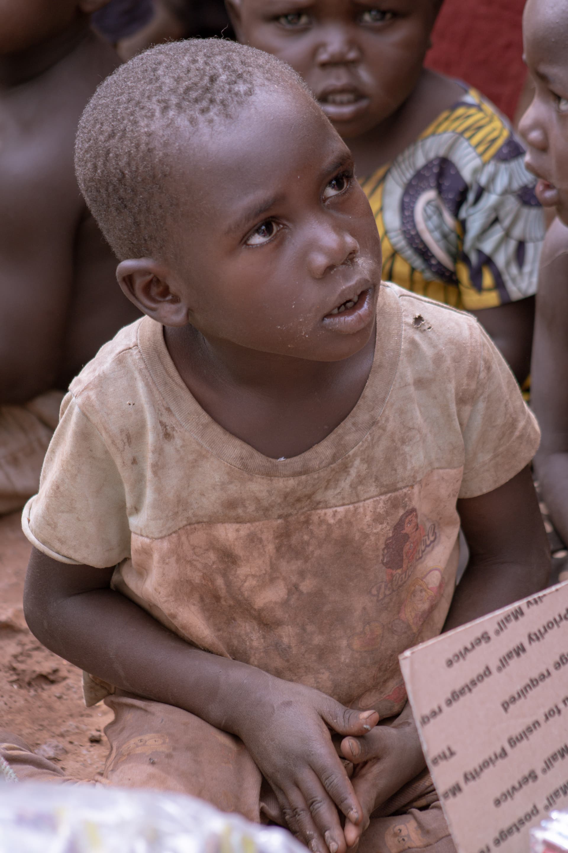 A young boy looking up while holding a piece of paper or card in a dry field.