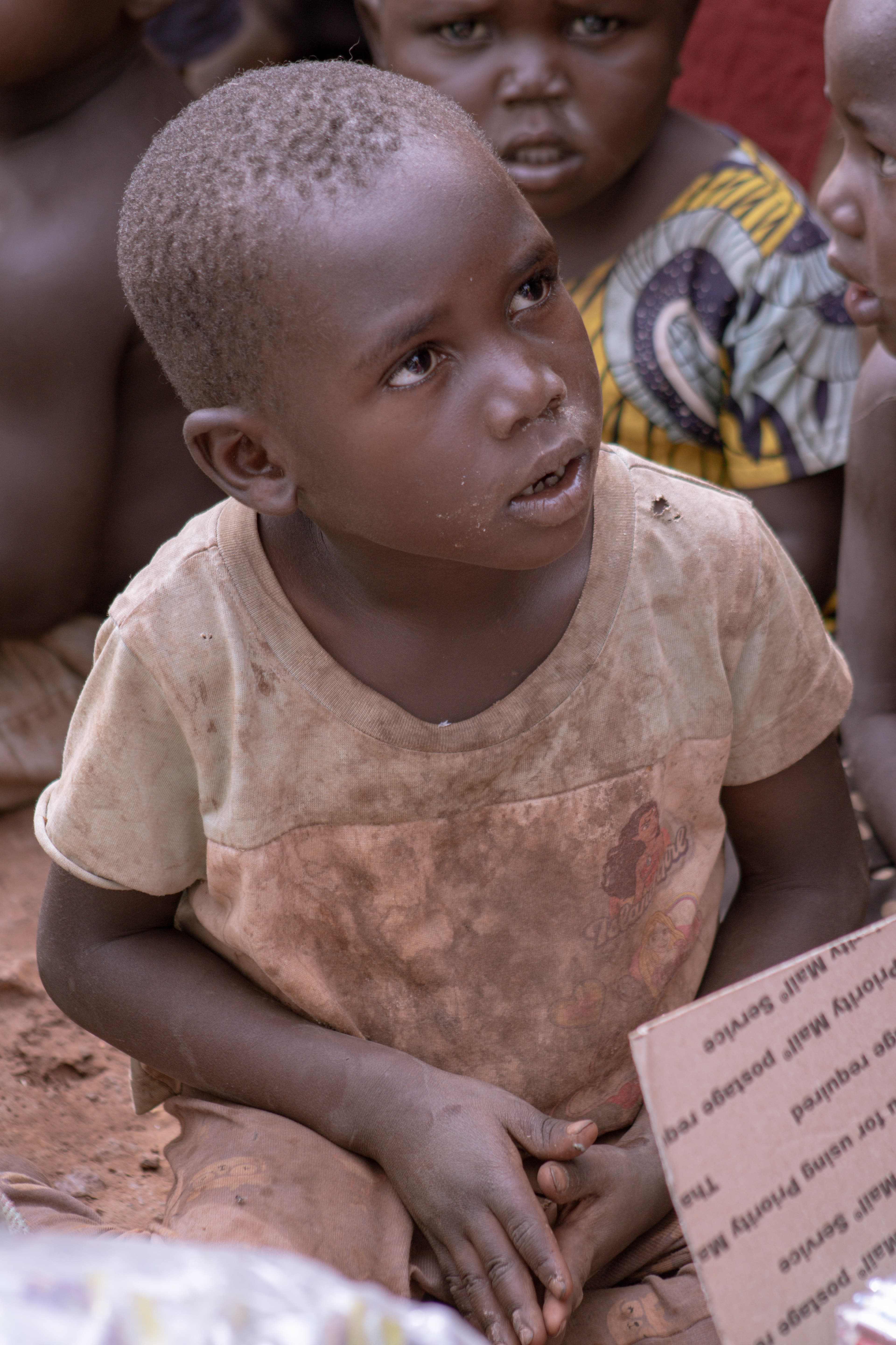 A young boy looking up while holding a piece of paper or card in a dry field.