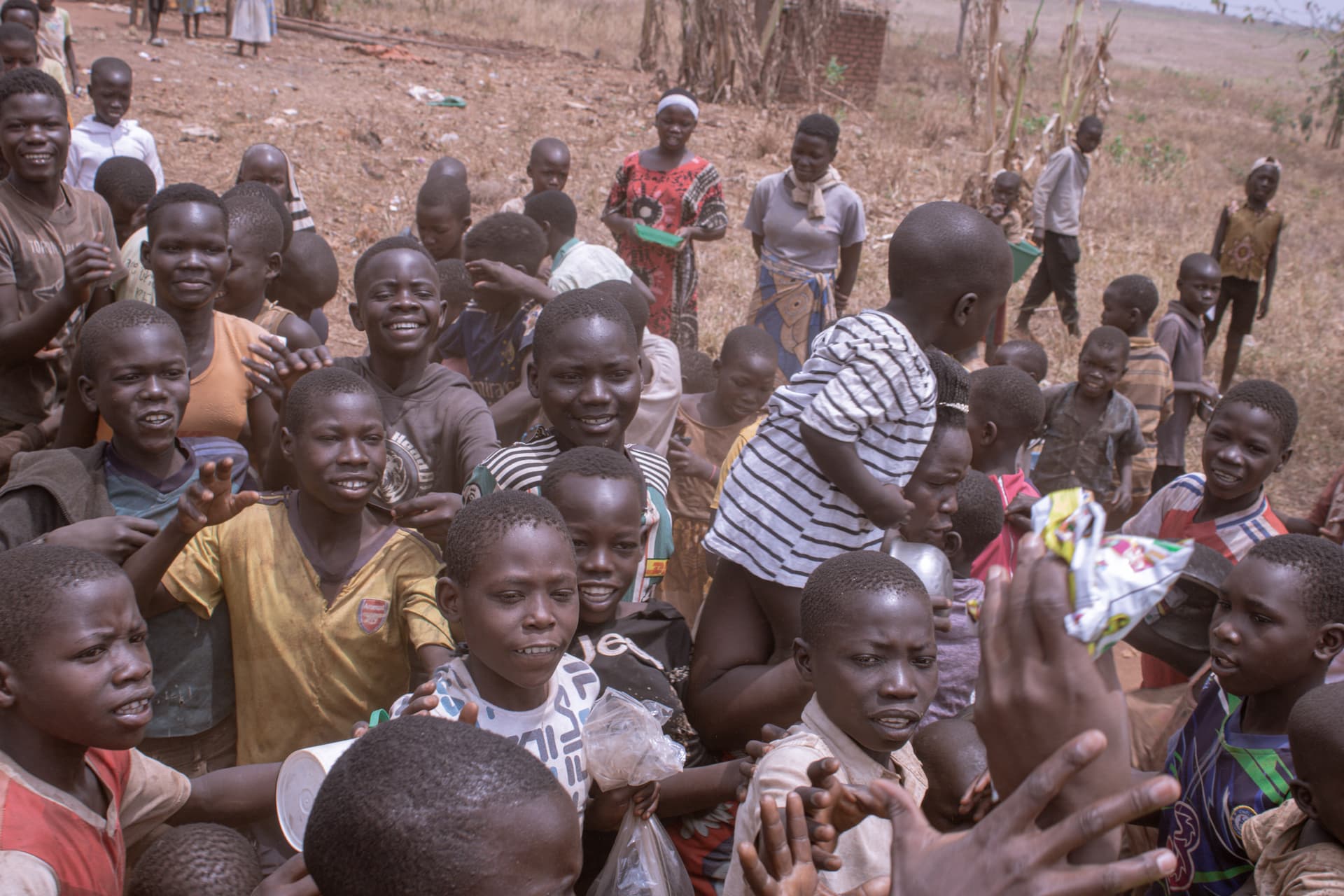 A group of children gathered together, some waving, in front of a rural homestead.