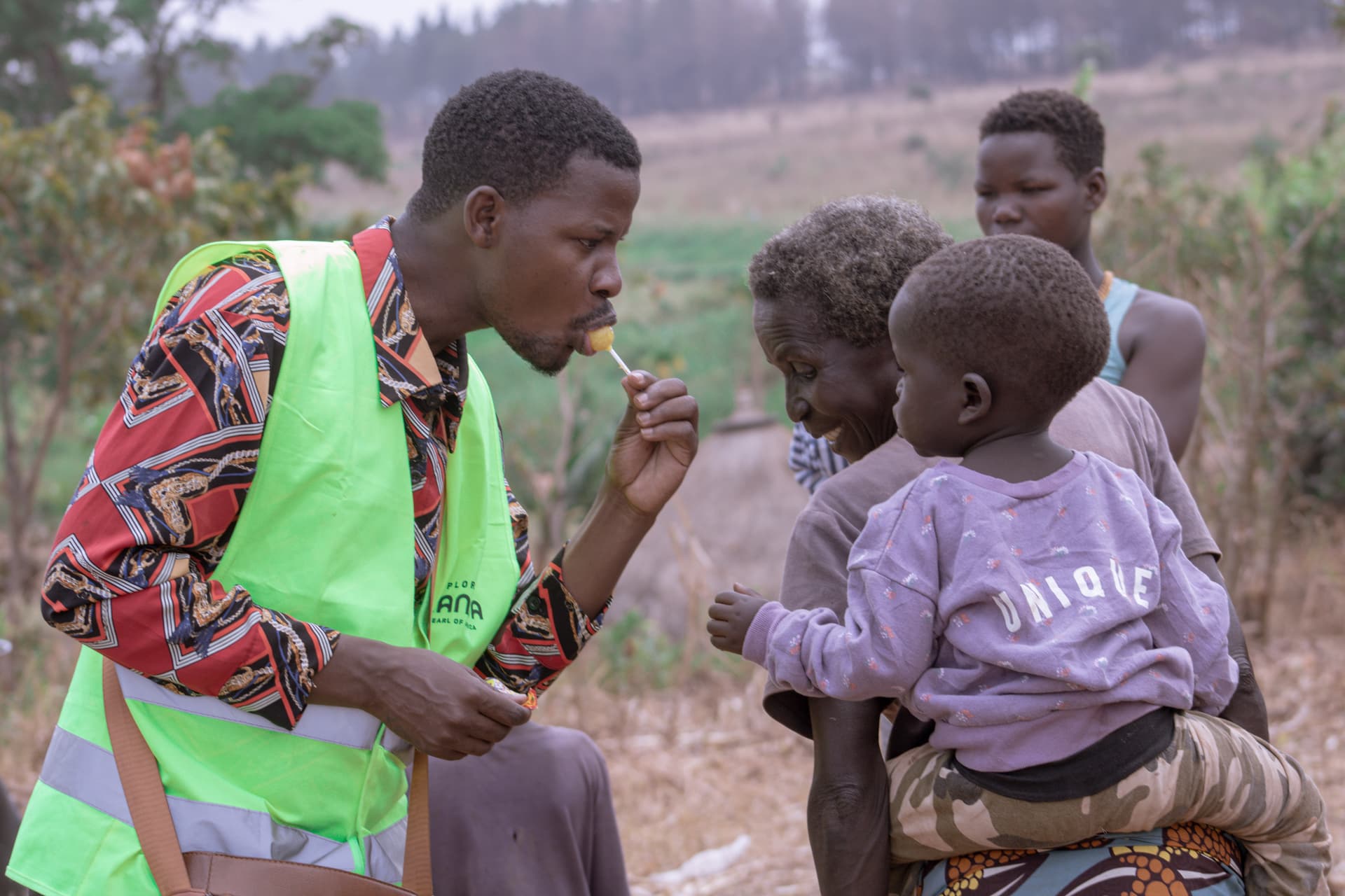 A man in a high-visibility vest kneeling to talk with two young children outdoors.