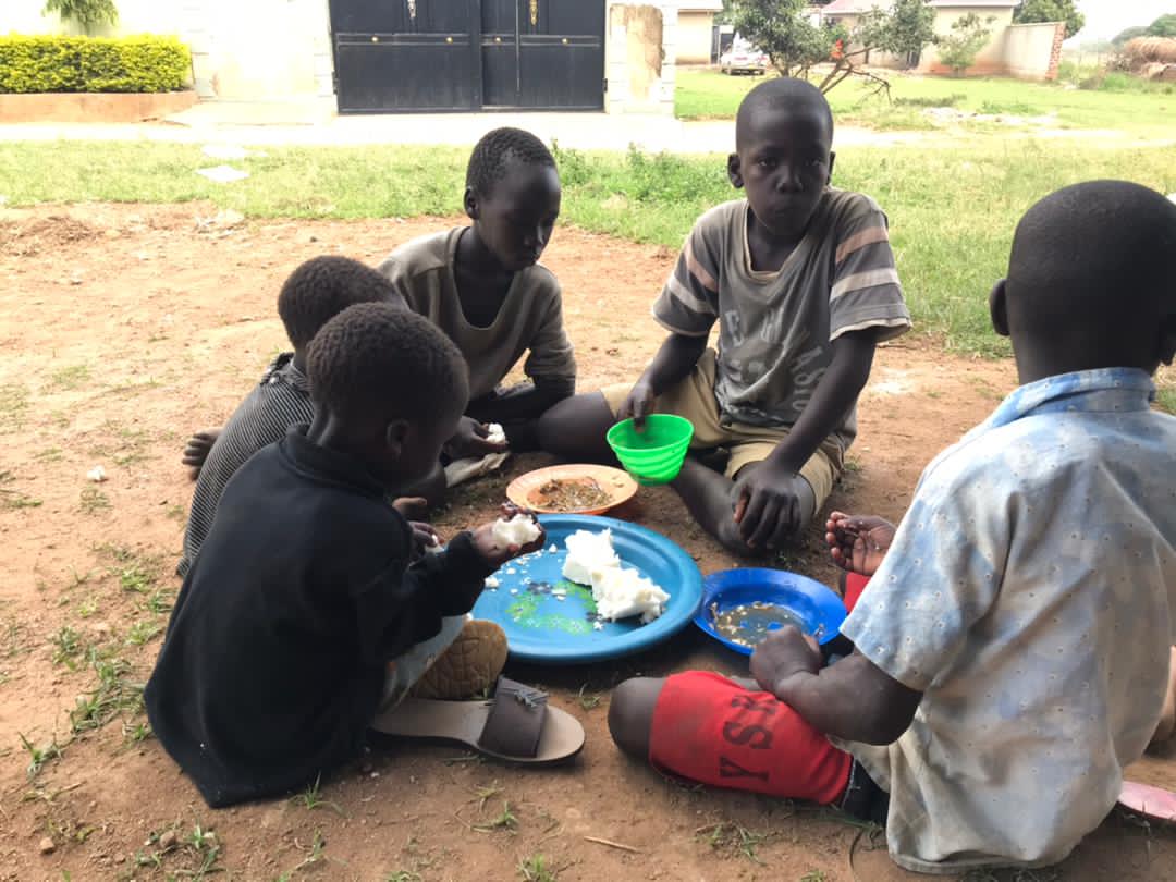 Children sitting outdoors on the ground eating a meal from plates.