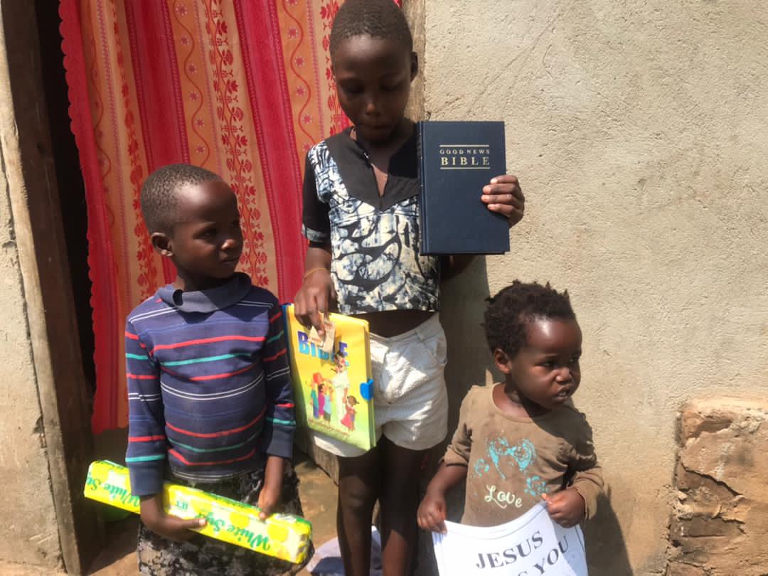 Boy holding a Bible and a toddler holding a coloring book standing against a red curtain backdrop.