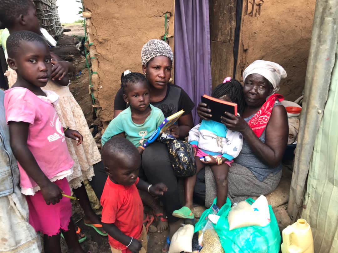 Woman and children standing in a doorway holding food items and a Bible at Bukuuba landing site.