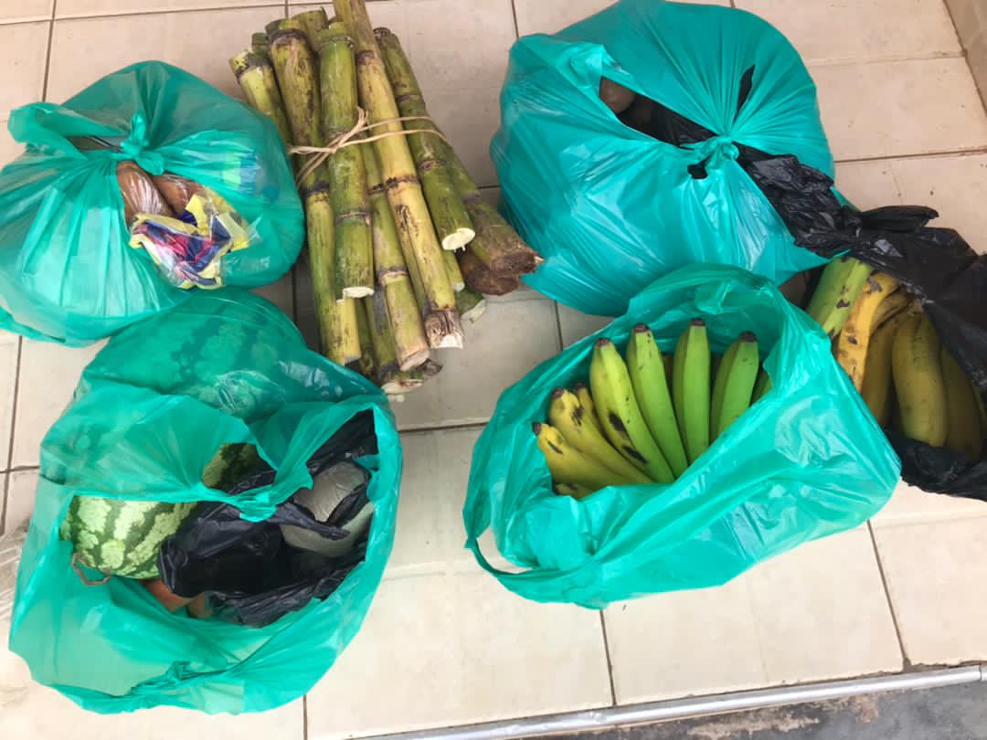 Green relief bags filled with matooke bananas arranged on a tiled floor ready for distribution.