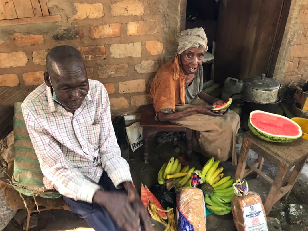 Elderly man and woman sitting indoors together as she eats a slice of watermelon.
