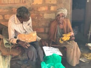 Elderly couple Shaban and Joeria sitting together indoors near a brick wall with their food gift.