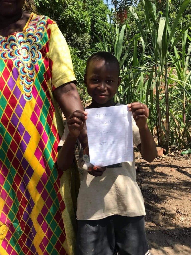 Mother and children indoors, one child holding a blank sheet of paper during a home visit.