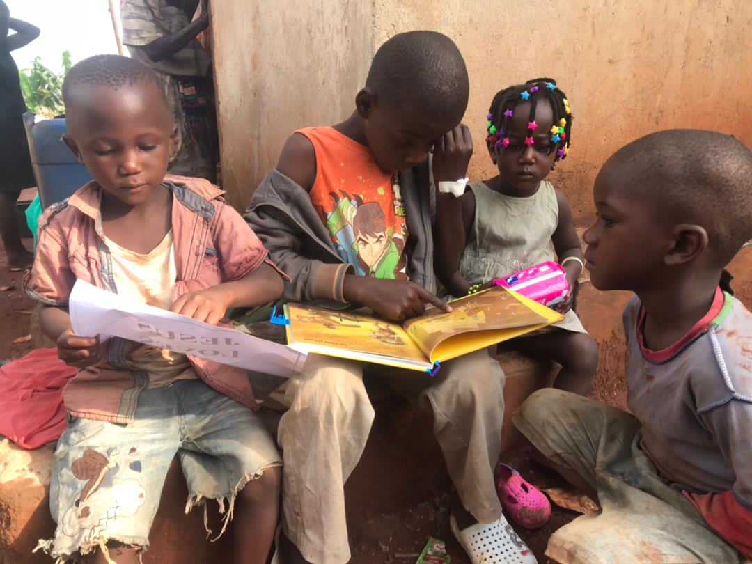 Children sit together outdoors reading an open picture Bible book.