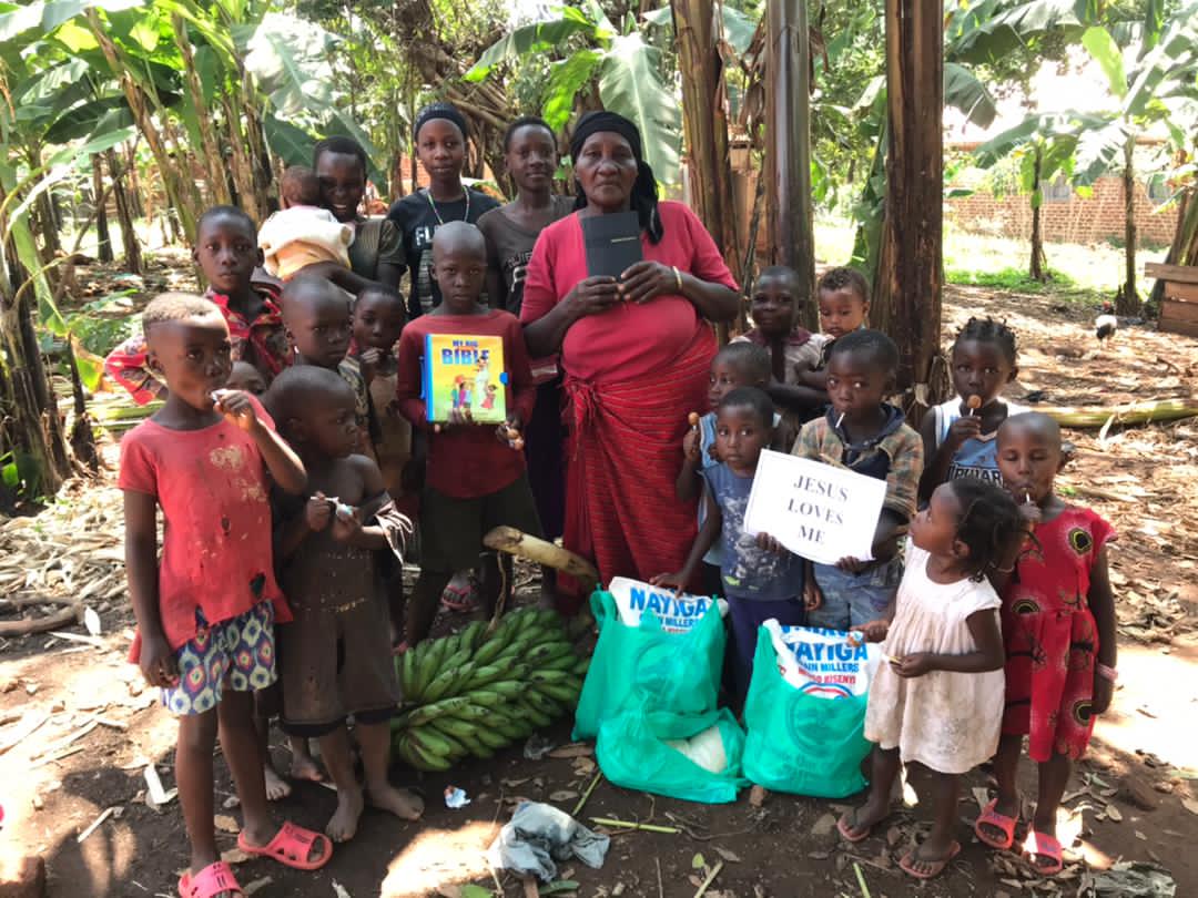 A woman stands with a group of children outdoors, holding relief bags filled with bananas.