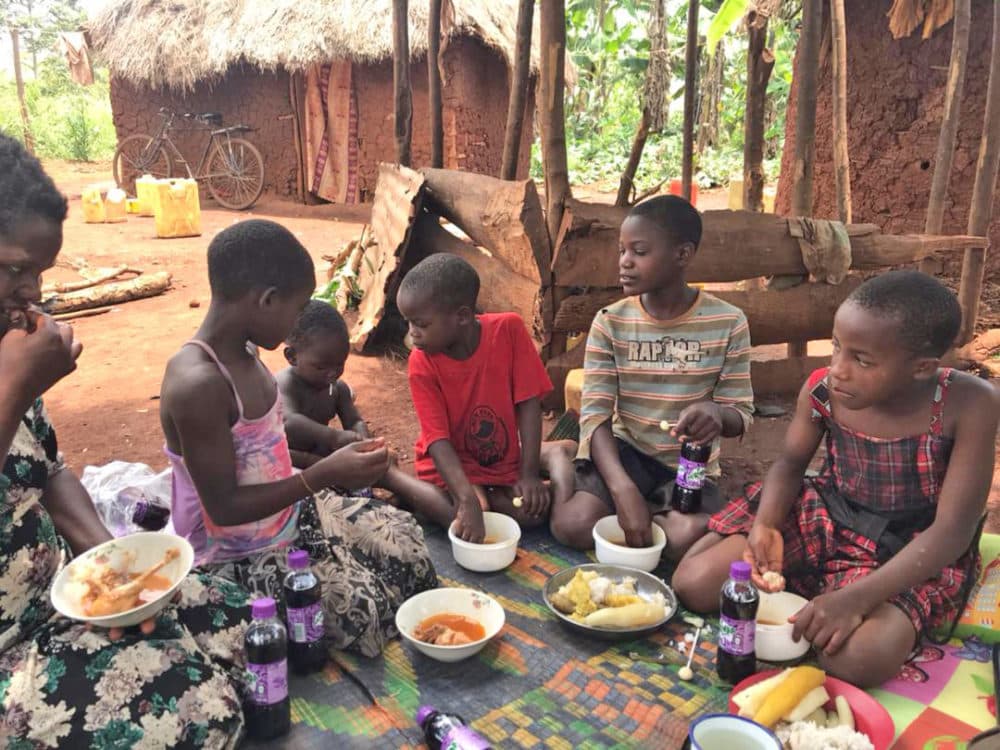 Mrs. Rossetti's family sitting together on a mat outdoors sharing a meal.