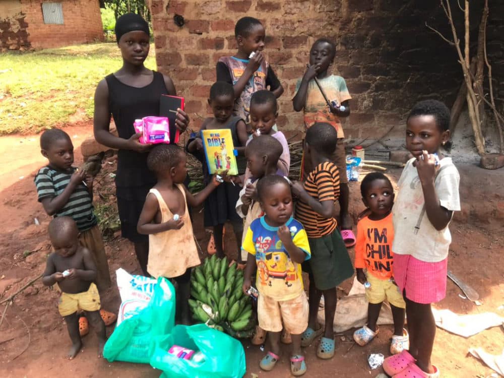 Group of Ugandan children standing outdoors beside a bunch of matooke bananas and a food relief bag.