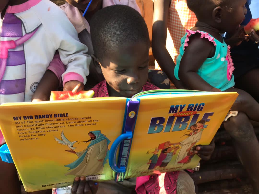 Children sit outdoors holding new My Big Bible board books.