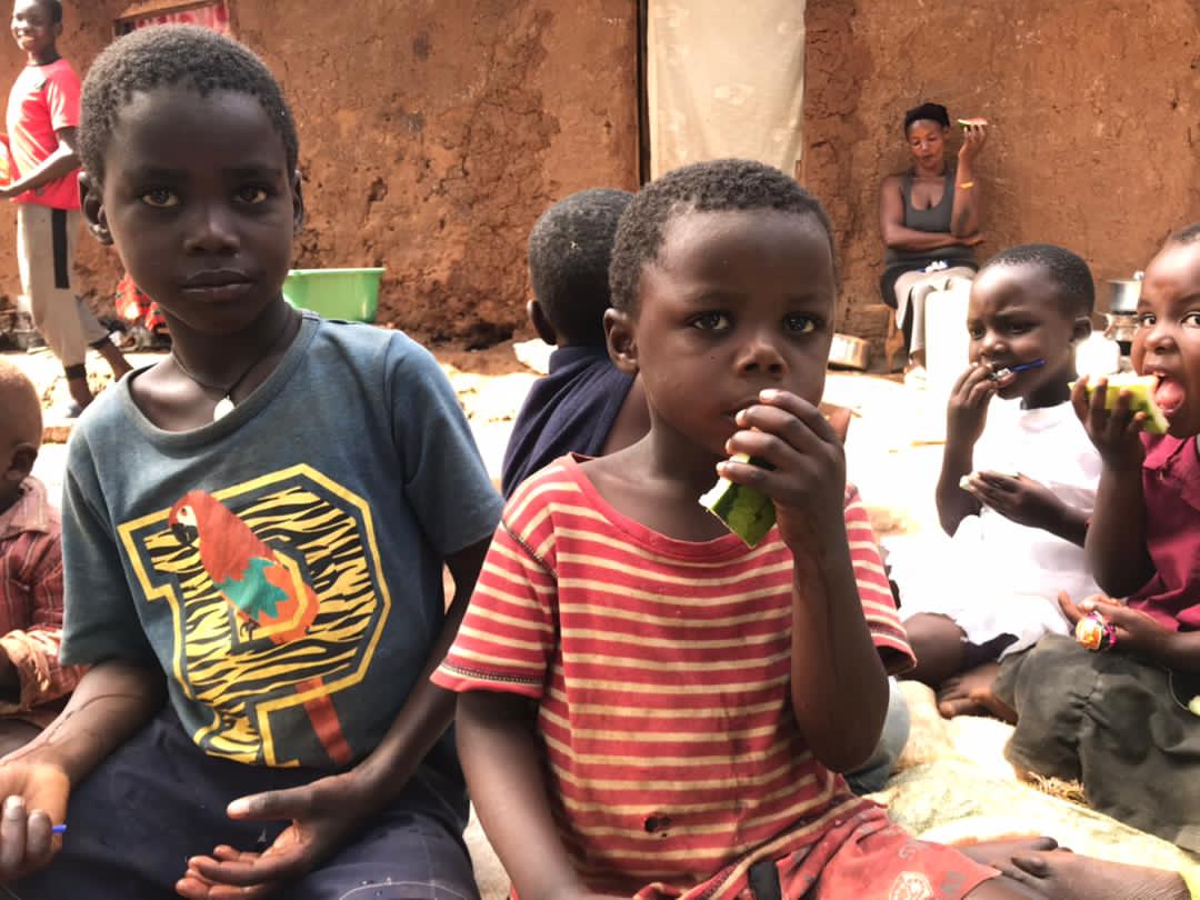 Two boys sit on the ground eating bananas together with other children nearby.