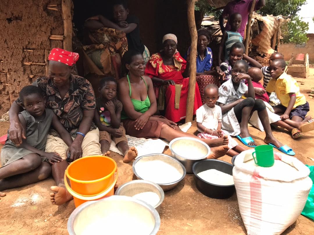 A family sits on the ground with metal bowls and basins of white posho they have received.