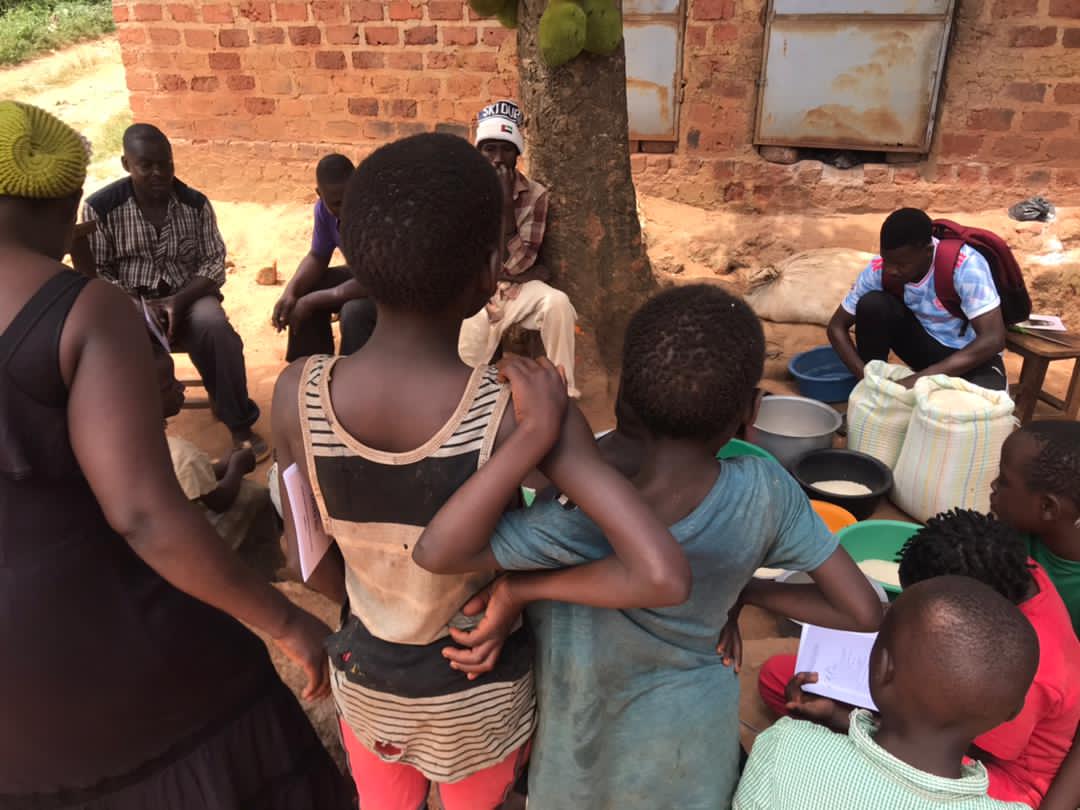 Group of women and children gathered around jerrycans and bowls near a brick house
