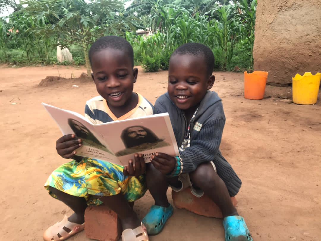 Two girls seated together reading a gospel tract booklet with a portrait of Jesus