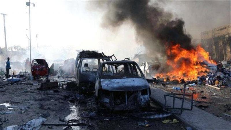 News photo of burning vehicles and smoke on a city street after an explosion in Kampala