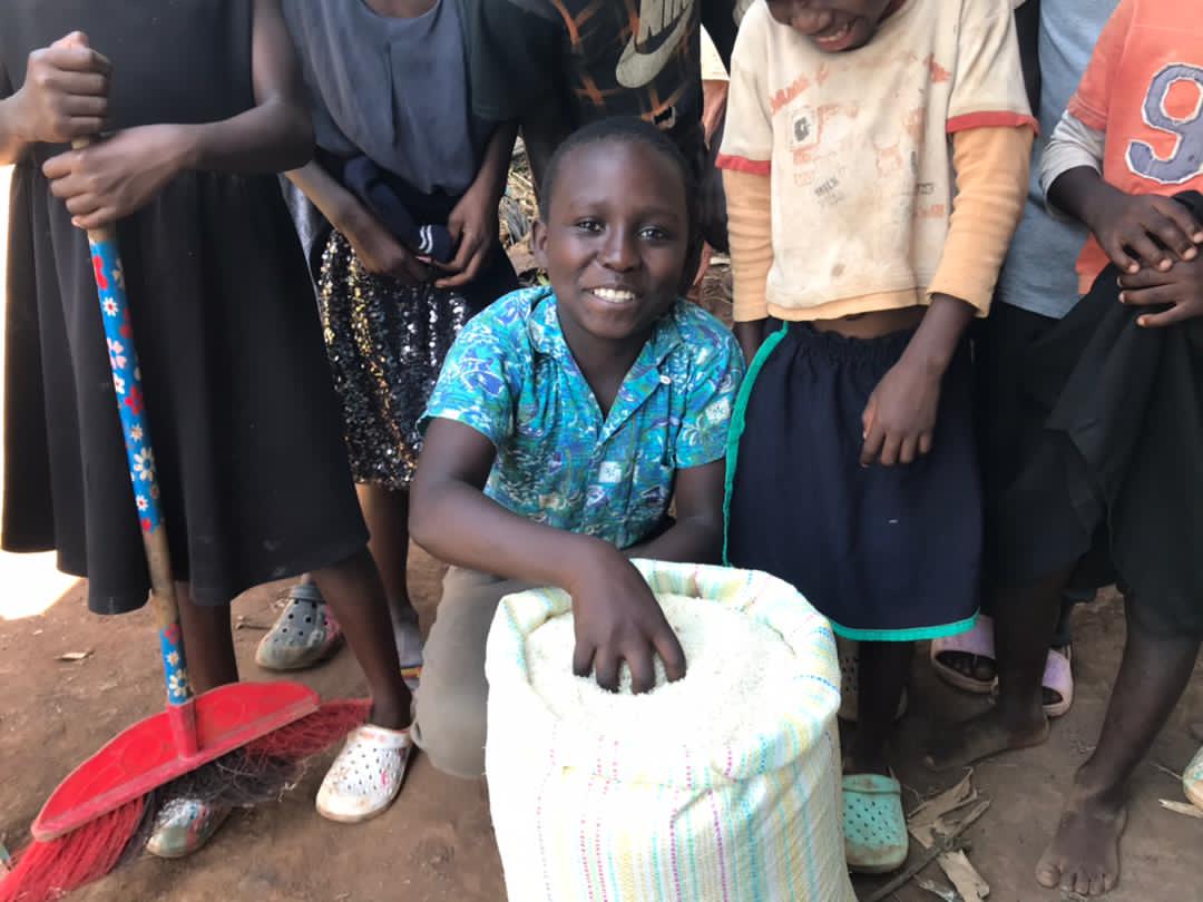 Girl smiling while sitting with a sack of food, holding a gospel tract with a portrait of Jesus