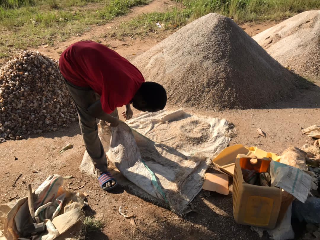 Person in a red shirt bent over breaking rocks at a stone quarrying site