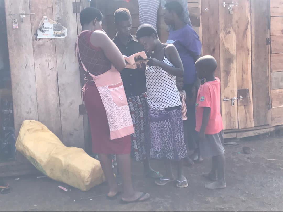 Woman and children gathered outside a wooden shop with a yellow sack on the ground