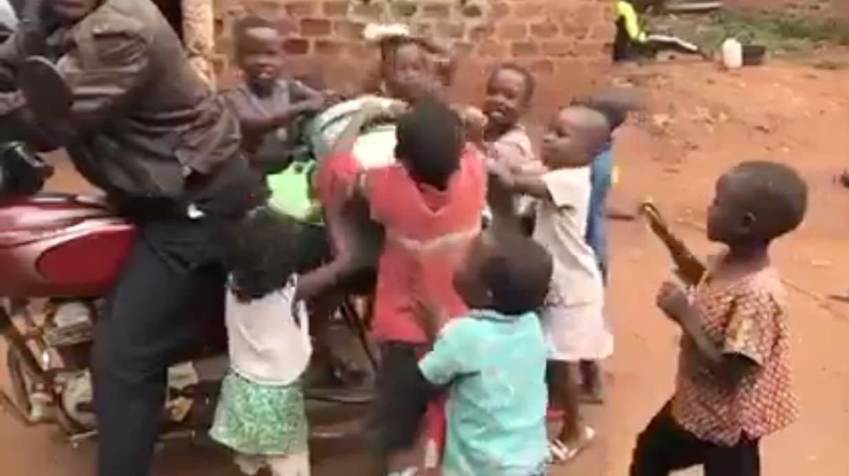 Group of children reaching toward an adult near a brick wall in a rural compound