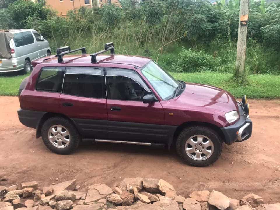 A maroon SUV with a roof rack, JFM's new food delivery vehicle, parked on a dirt road.