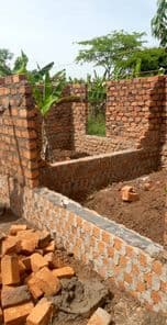 Partially built brick house walls under construction with loose bricks piled on the ground.