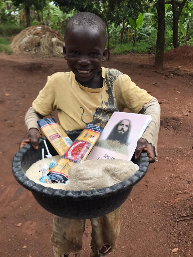 Boy holds a large basin of rice and gospel tracts on a dirt path in Uganda