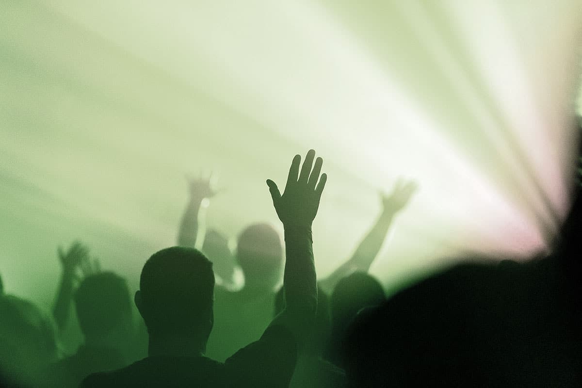 Silhouetted crowd with hands raised in worship, backlit by green stage lighting, a stock-style graphic.