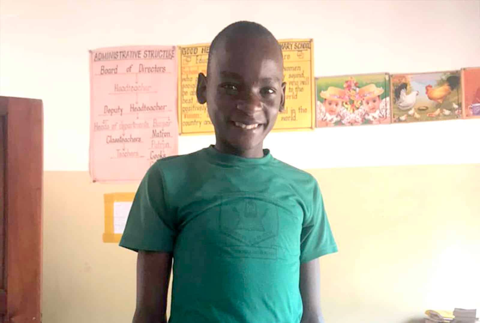 Eric, a teenage boy in a green school shirt, smiles for a portrait inside a primary seven classroom.