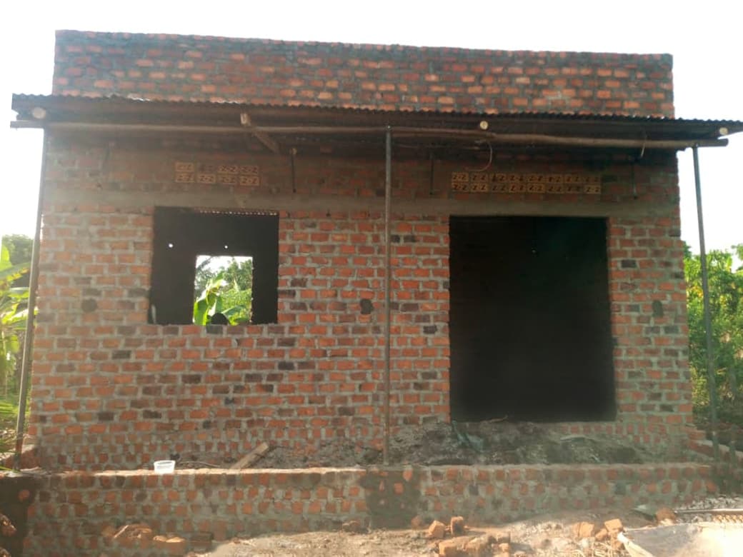 A partially built brick house with a metal roof and open doorway stands under construction.