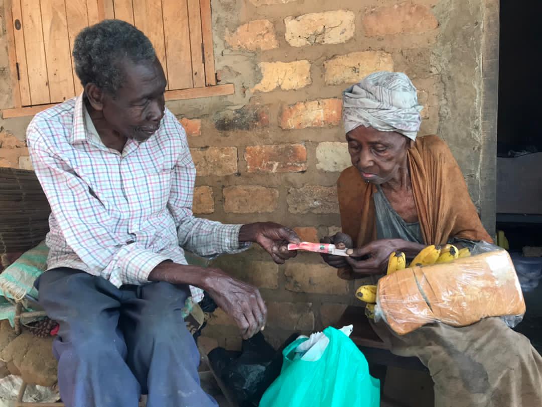 Shaban hands an item to his wife Joeria as they sit together indoors, a green bag nearby.