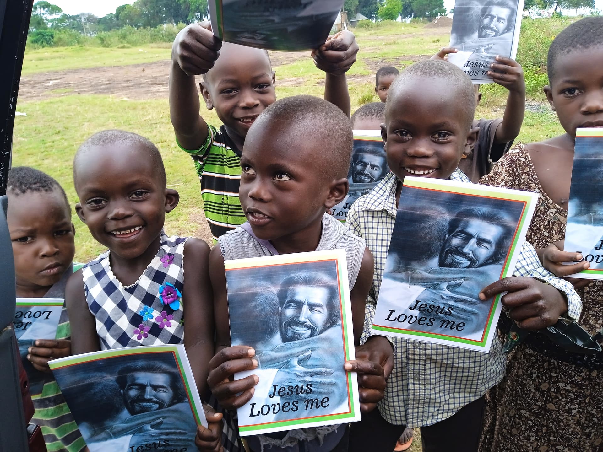 Group of children outdoors hold up open photo booklets and cheer in a field.