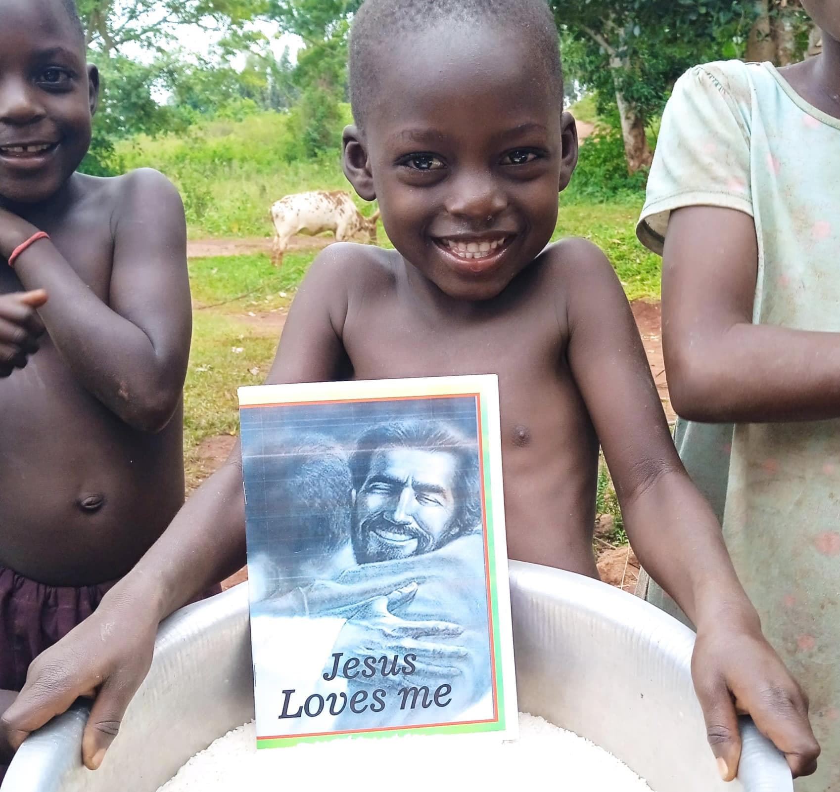 A shirtless boy smiles while holding a basin containing a gospel tract, other children nearby.