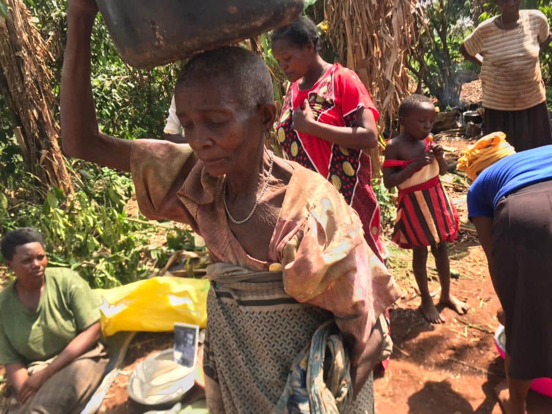 Granny Angella carries a large bundle on her head while walking a dirt path with children.