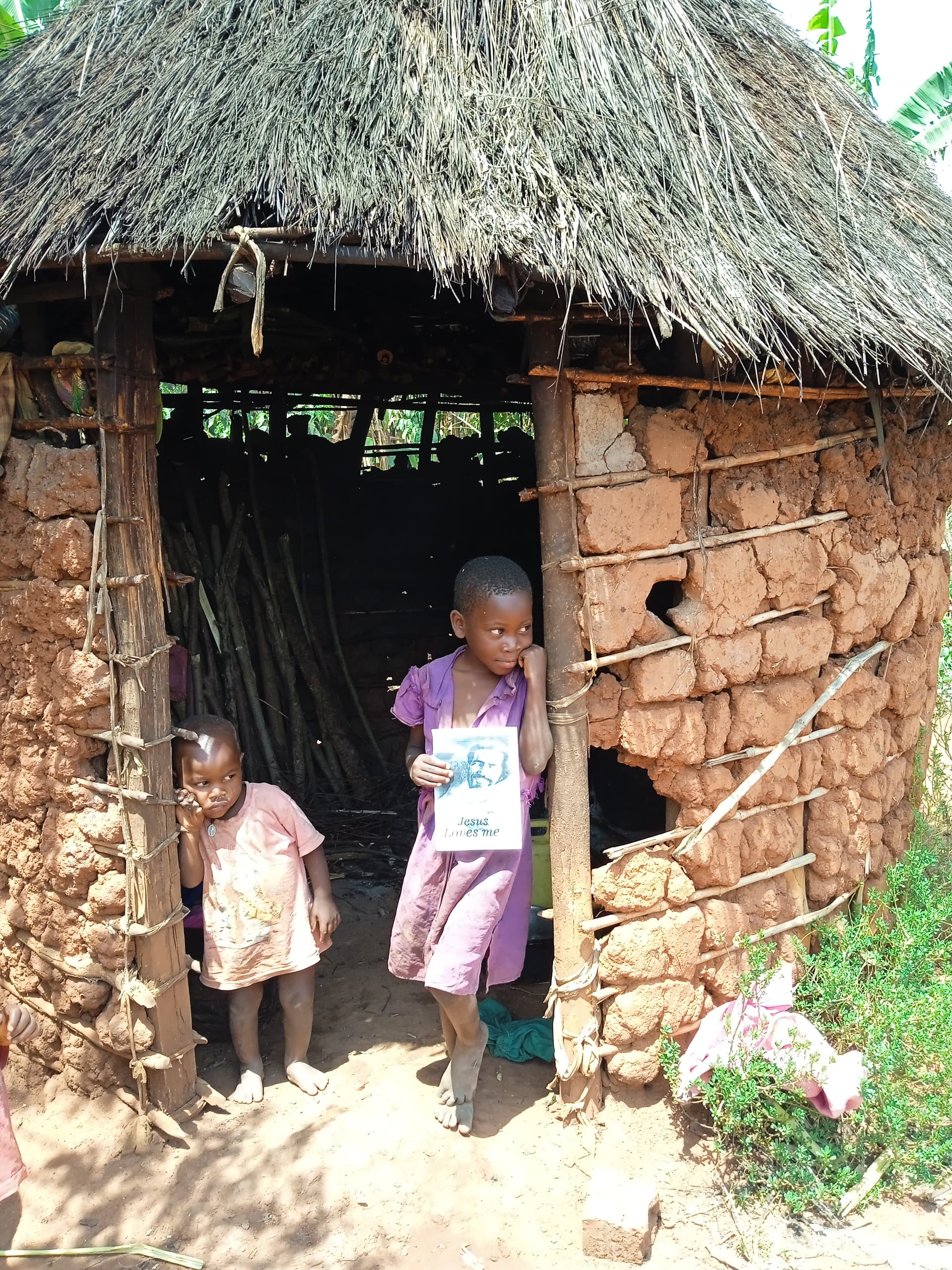 A young girl stands in the doorway of a mud-brick hut.