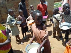 Aerial view of children lined up outdoors holding empty bowls for a JFM food handout.